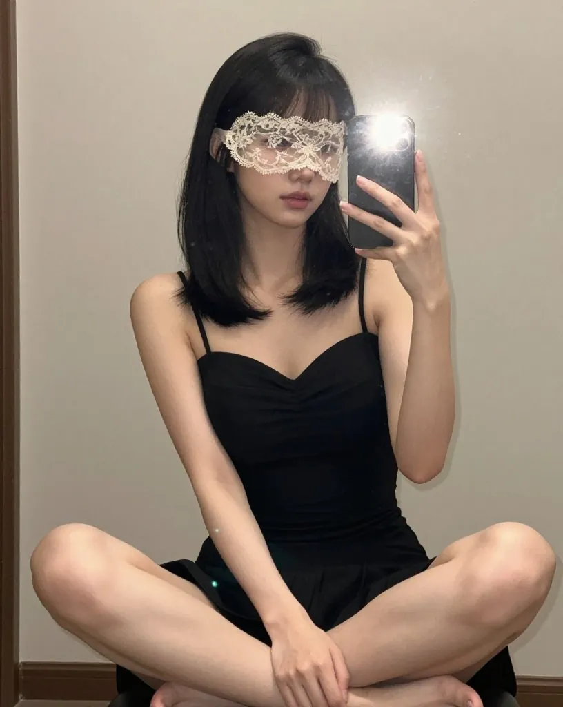 흰 레이스 가면을 쓰고 검은 끈 원피스 차림으로 바닥에 책상다리로 앉은 여성